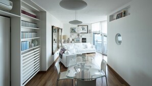 Un salon moderne avec une table à manger en verre, des canapés blancs et une bibliothèque.