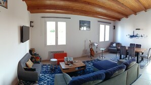 Ein Wohnzimmer mit einer Couch, einem Couchtisch, einem Esstisch mit Stühlen, einer Gitarre und einem Bild an der Wand.