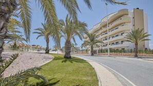 A modern building with multiple balconies, a curved road, and palm trees. - Apartment 'Bahia' with Shared Pool, Wi-Fi and Air Conditioning (Els Arenals del Sol)