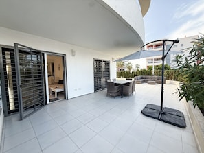A modern outdoor patio with a dining table and chairs, a large umbrella, and a sofa.