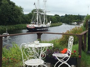 A river with a sailing ship, a small boat, and a white metal table with chairs. - Charming 2-bedroom cottage in Inverness perfect for relaxing stays (Inverness)