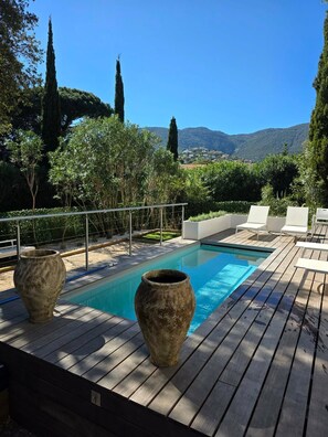 Ein Pool mit zwei großen Vasen, umgeben von einer Holzterrasse und weißen Liegestühlen, mit Blick auf eine Berglandschaft im Hintergrund.