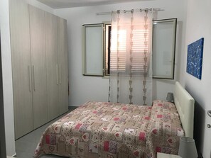 Ein Schlafzimmer mit einem Bett, einem Kleiderschrank, einem Fenster mit Vorhängen und einer Wandlampe.