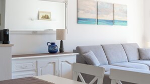 Una habitación moderna con un equipo de aire acondicionado blanco, una mesa de comedor con un mantel individual marrón, un sofá y una cafetera sobre una encimera.