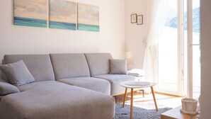 Un salón moderno con un sofá gris, una mesita redonda y vista al mar a través de un ventanal grande.