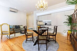 A modern living room with a dining table, chairs, a chandelier, a sofa, and a kitchen in the background. - Azzulea Avenida21 Historic Charm, Modern Luxury (Lisbon)