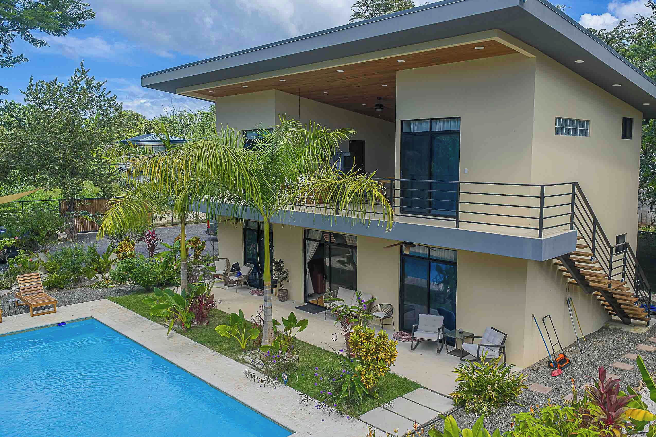 Uma casa moderna de dois andares com piscina, área de estar externa e escadaria que leva a uma varanda.