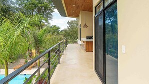 A modern balcony with a pool, wooden ceiling, and a dining area with bar stools. - Walk to beach, 2BR/2BA, Apartment, pool, parking, outdoor kitchen (Playa Grande)