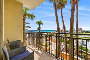 Ein Balkon mit Korbmöbeln, Palmen und Blick auf das Meer und die Stadtlandschaft.