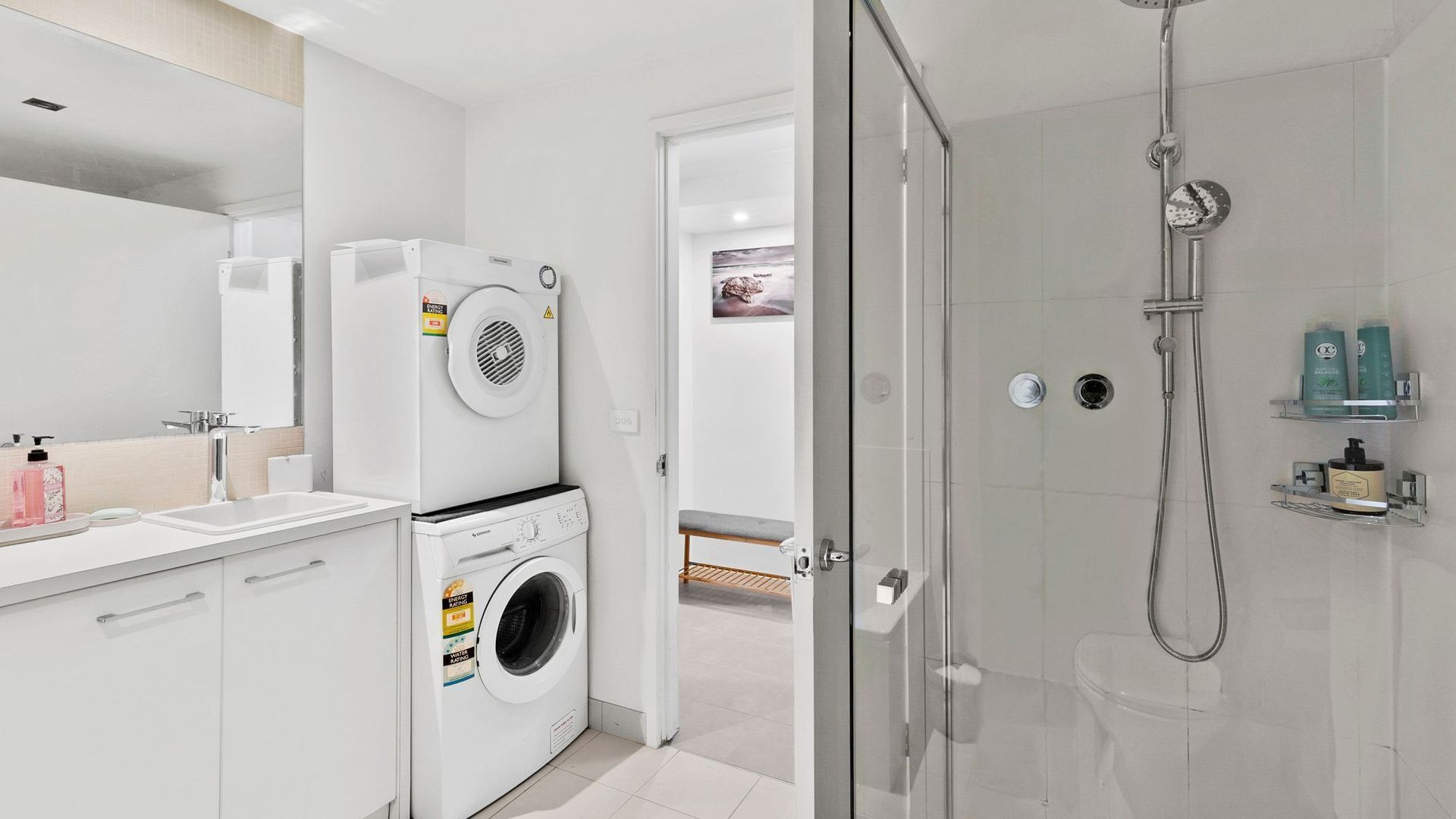 A modern bathroom with a glass shower enclosure, a washing machine, and a toilet.