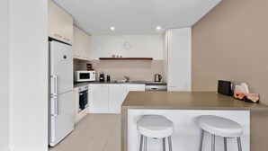 Una cucina moderna con mobili bianchi, un forno a microonde, un bollitore e una sveglia appesa al muro. Due sgabelli da bar bianchi sono posizionati al bancone.