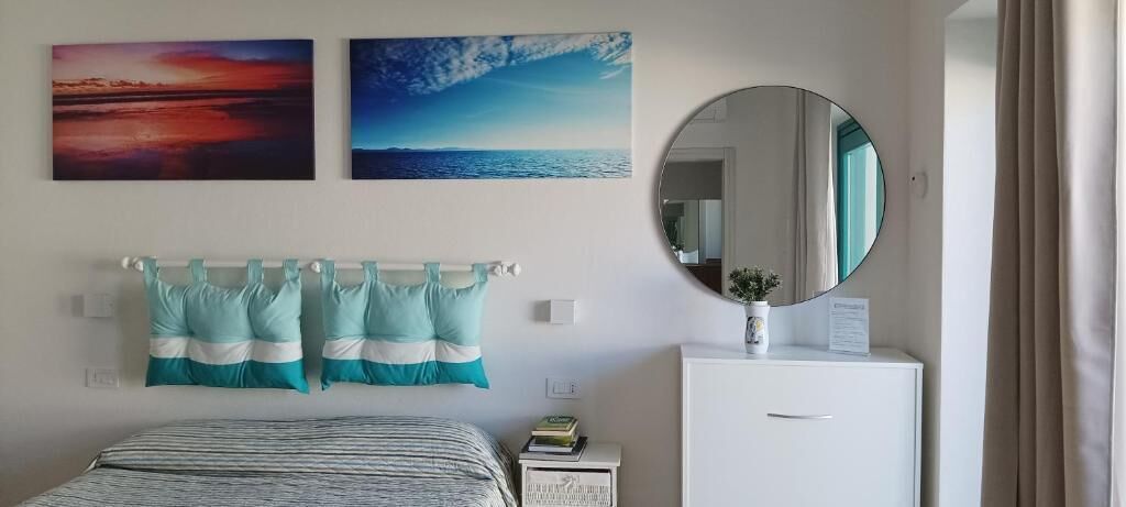 Una camera da letto con un letto, un comodino, una cassettiera, uno specchio rotondo e due quadri appesi al muro.