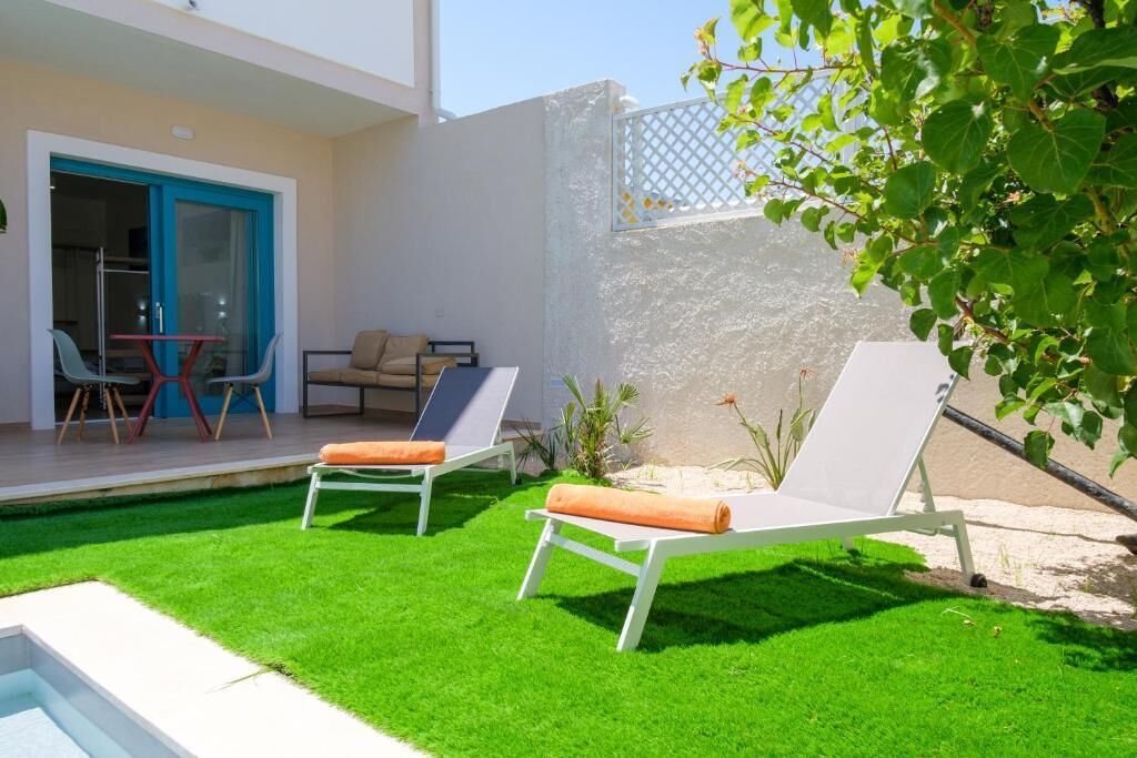 Zona de piscina amb dues gandules, una taula i seients, i entrada d'edifici amb una porta blava.