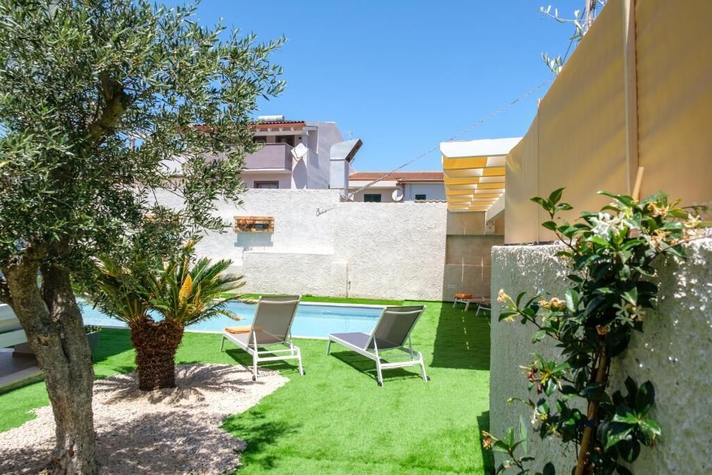 A pool area with two lounge chairs, a palm tree, and a white wall.
