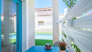 Uma varanda com vista para uma piscina, uma mesa com xícara e pires, e um vaso de planta.