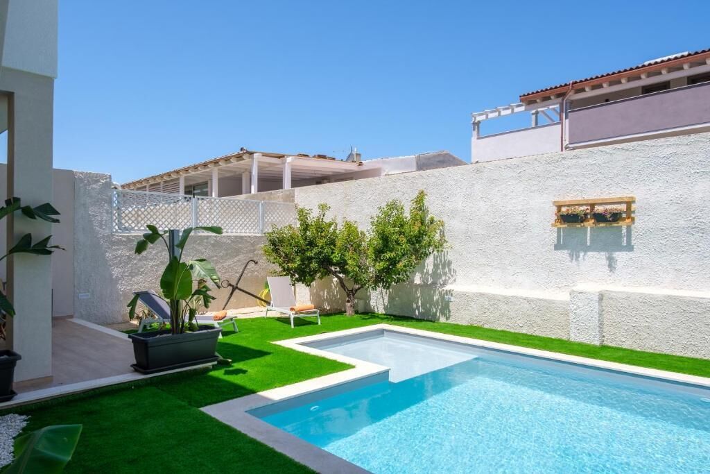 Piscina amb una paret blanca i un petit jardí amb una cadira i plantes.