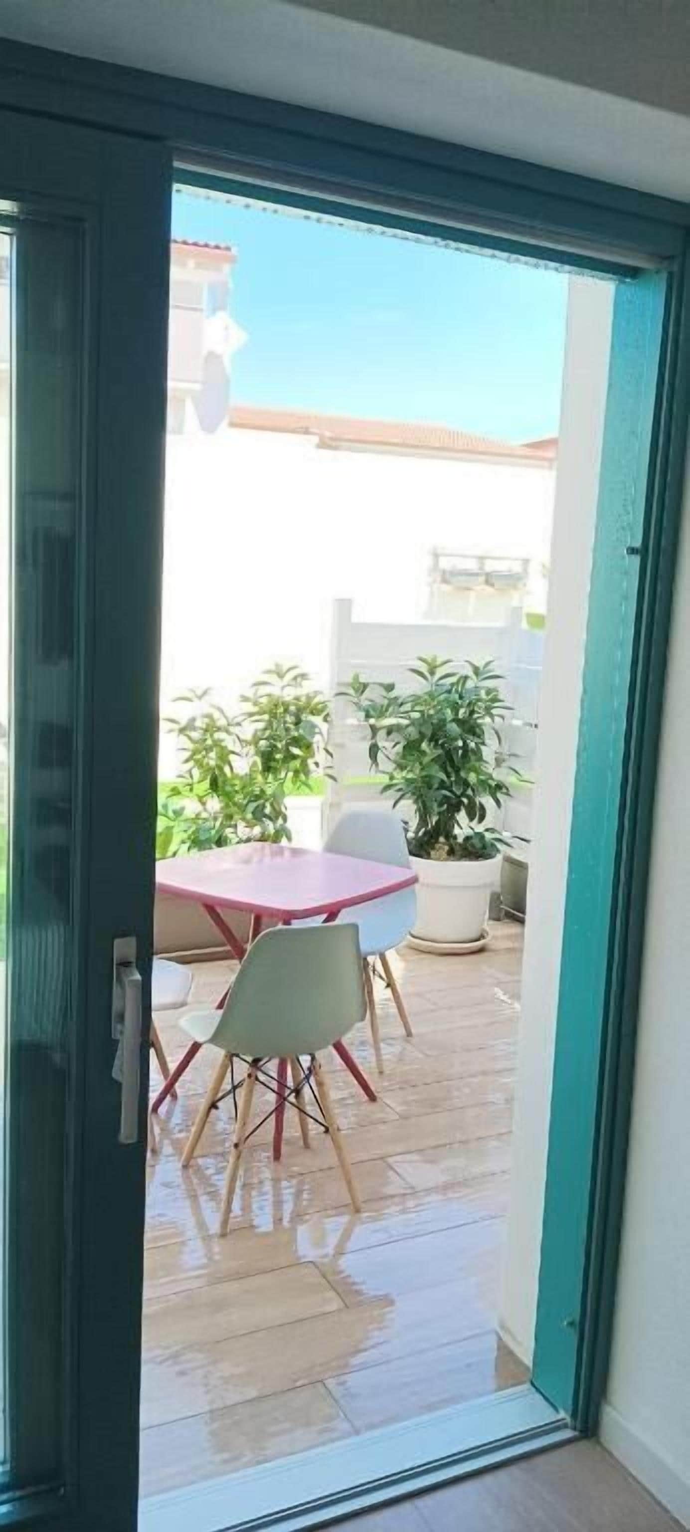 An open door leading to an outdoor patio with a table and chairs, potted plants, and a clear sky.