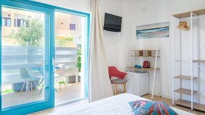 Quarto com cama, escrivaninha, cadeira, televisão e vista para o exterior.