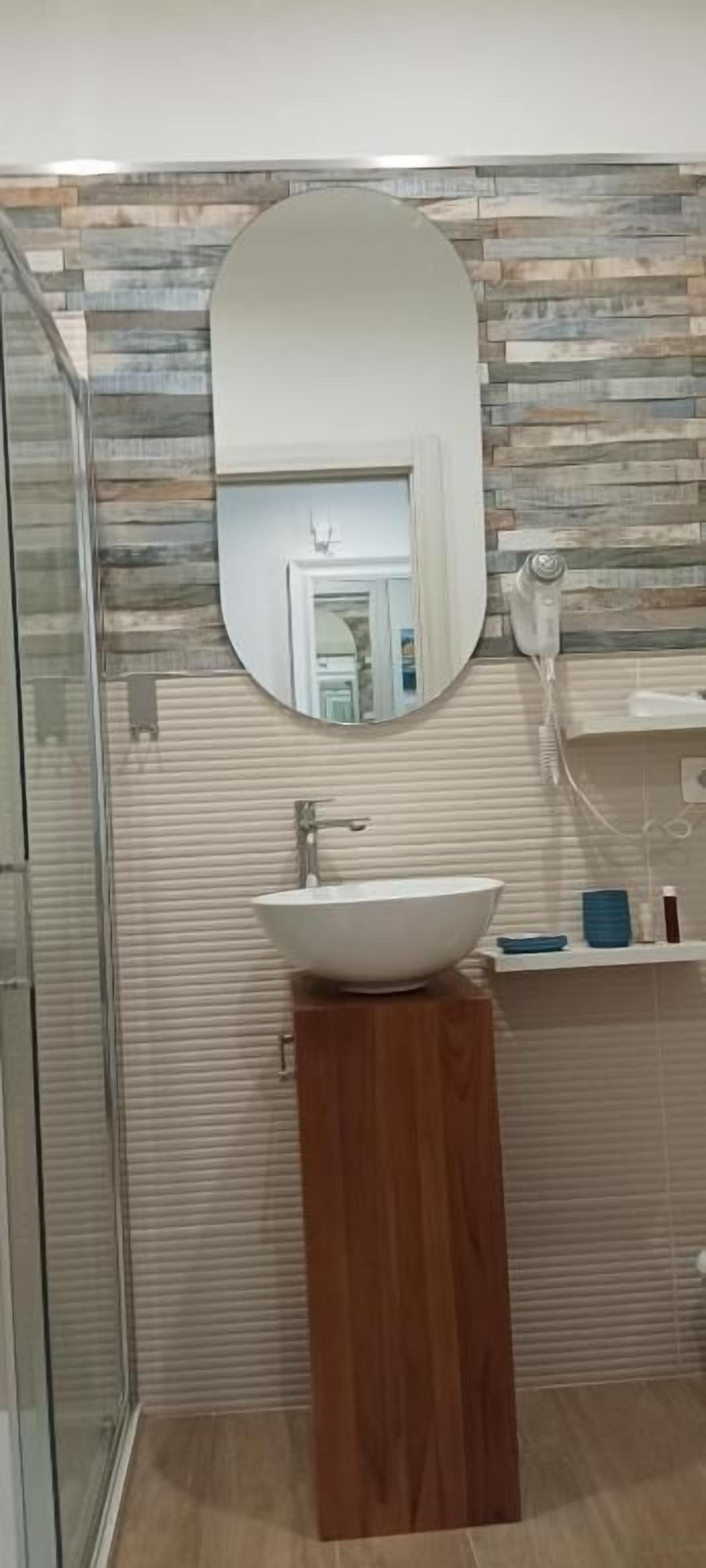 Casa de banho com toucador de madeira, lavatório branco, espelho e secador de cabelo numa prateleira.