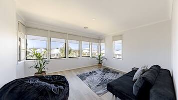 A spacious room with a large window, a black sofa, a patterned rug, and two potted plants.