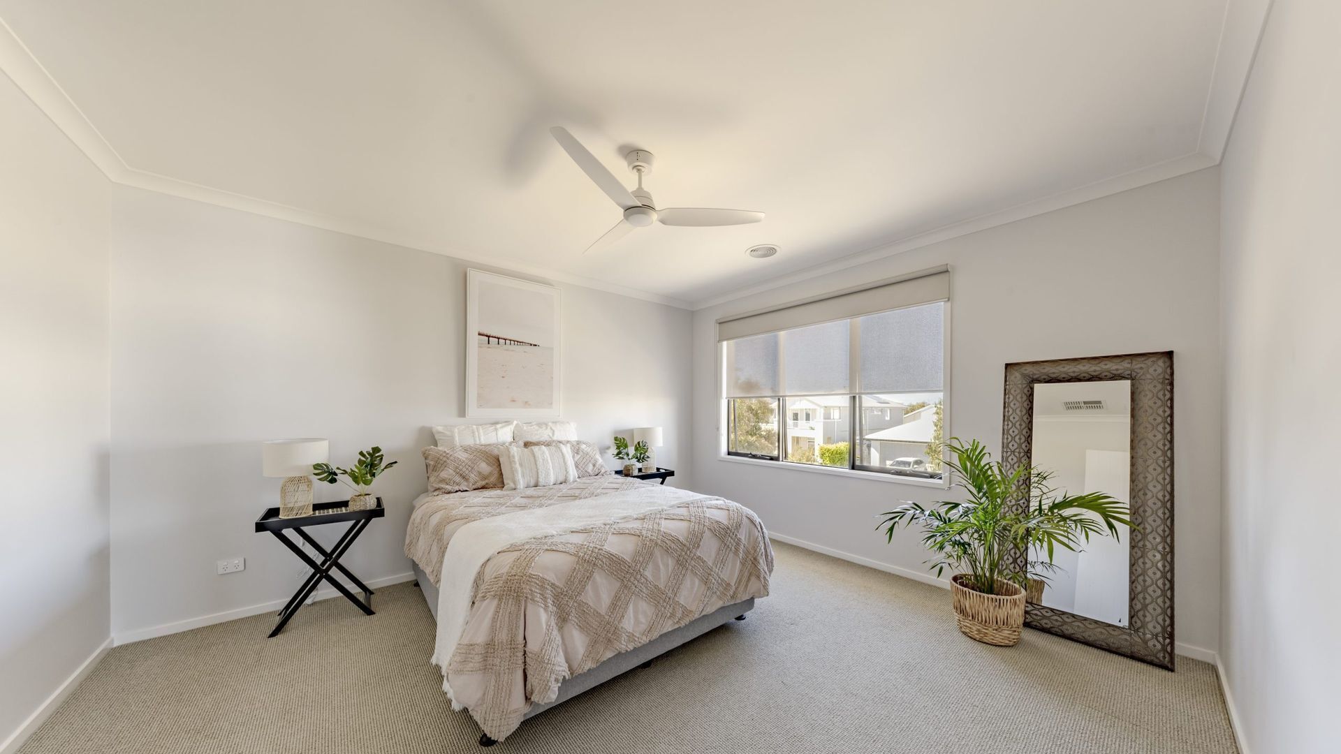 A bedroom with a bed, a ceiling fan, a window, and a mirror.