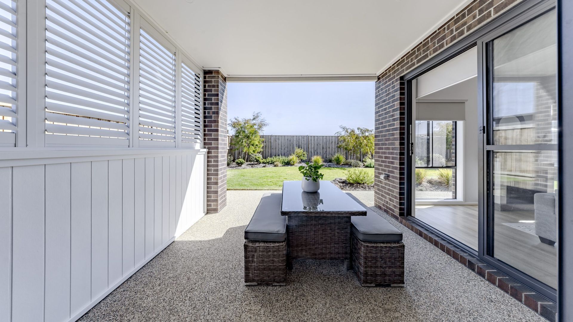 A patio with a table and chairs, a potted plant, and a view of a backyard with a wooden fence and greenery.