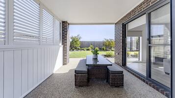 A patio with a table and chairs, a potted plant, and a view of a backyard with a wooden fence and greenery.
