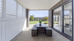 A patio with a table and chairs, a potted plant, and a view of a backyard with a wooden fence and greenery. - Banksia Retreat a family friendly beautiful home in The Point estate (Point Lonsdale)