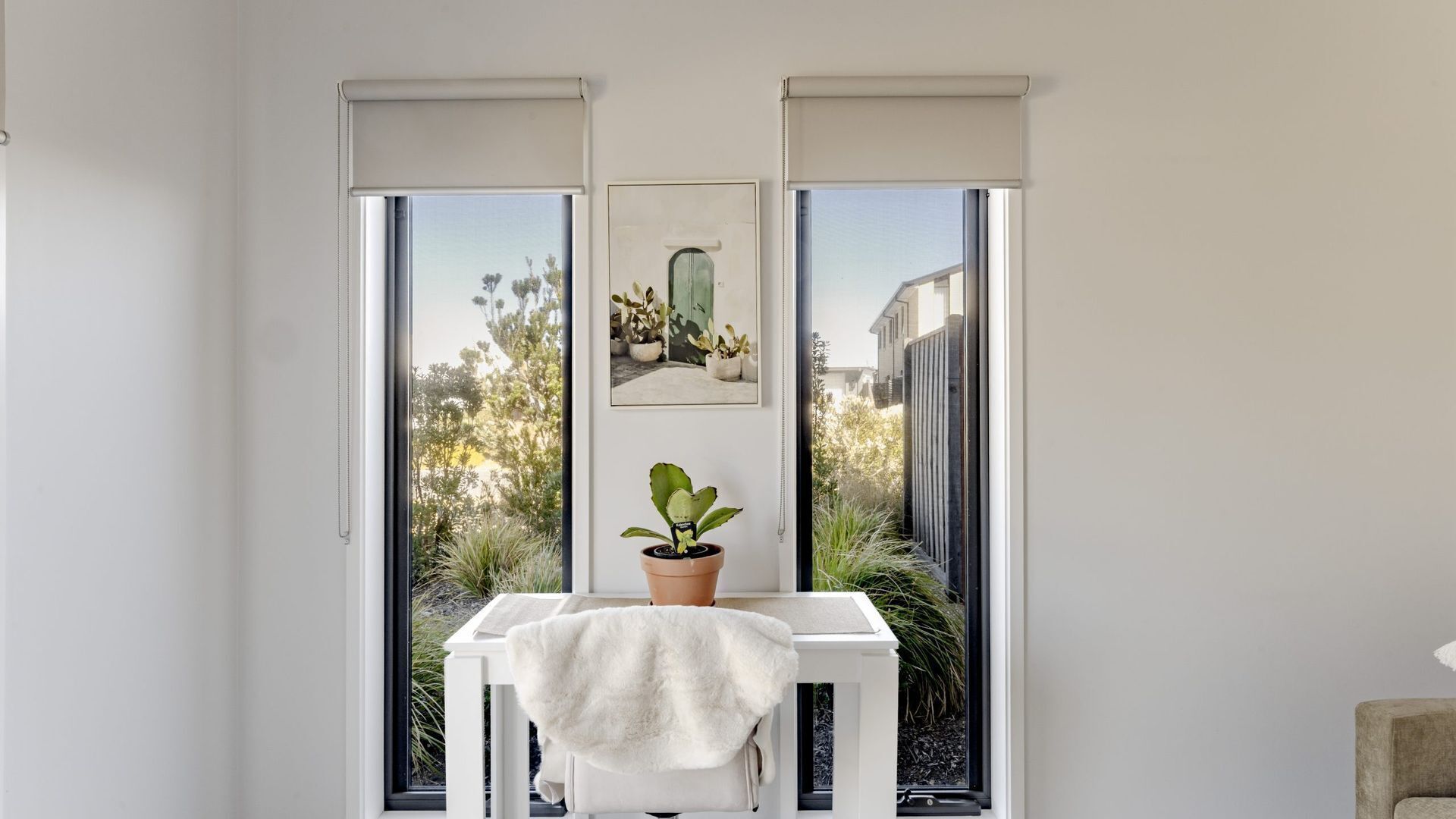 A room with a white table, a potted plant, and a framed picture on the wall.