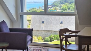 Ein Zimmer mit einem großen Fenster, einem Sofa, einem Sessel und einem Tisch.
