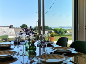 Mesa de comedor dispuesta con platos, vasos y un florero con flores, con vistas a un paisaje pintoresco.