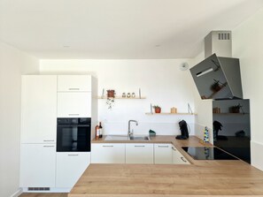 Uma cozinha moderna com armários brancos, forno preto, bancada de madeira, pia e coifa embutida.