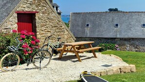 Ein Steinhaus mit roter Tür, einem Picknicktisch, einem Fahrrad und einem Surfbrett.