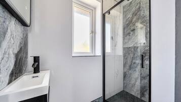 A bathroom with a white sink, a black faucet, a glass shower enclosure, and a window.