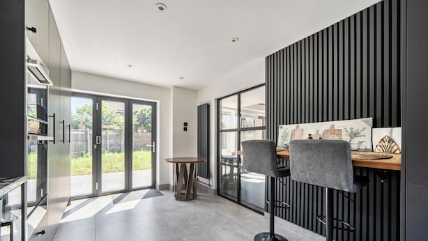 A modern kitchen with a dining area, large windows, and a view of the outdoors.