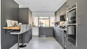 A modern kitchen with grey cabinetry, a wooden countertop, and a bar stool.