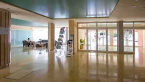Um hall amplo com balcão de recepção, área de estar e uma grande porta de vidro que dá para o exterior.