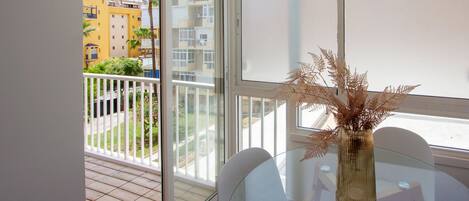 Un balcon avec une table en verre et un vase contenant des plantes séchées, donnant sur un quartier résidentiel.
