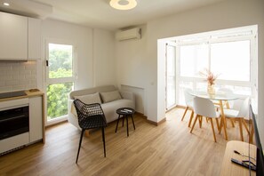 Une cuisine moderne dotée d’un four encastré, un coin repas avec une table et des chaises en verre, et un canapé avec un fauteuil noir.