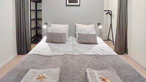 Ein modernes Schlafzimmer mit einem großen Bett, zwei Kissen, einem gerahmten Bild an der Wand und einer Stehlampe.