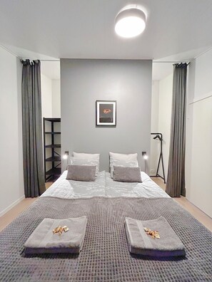 A modern bedroom with a large bed, two pillows, a framed picture on the wall, and a floor lamp.