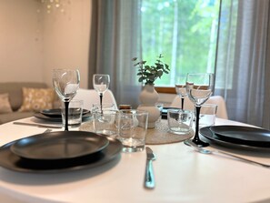 A dining table set with plates, glasses, and cutlery, with a vase of greenery and a window view in the background.