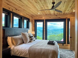 Ein Schlafzimmer mit einem großen Bett, mehreren Fenstern und einem Deckenventilator.