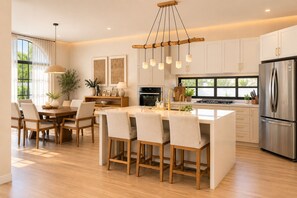 A modern kitchen with a central island, stainless steel appliances, and a dining area with chairs and a table. - Spacious and luxurious 4-bedroom house Playa del Carmen with AC (Playa del Carmen)