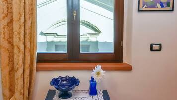 Ein Zimmer mit Fenster, Wandleuchte, einem gerahmten Bild und einem kleinen Tisch mit Vase und dekorativer Schale.