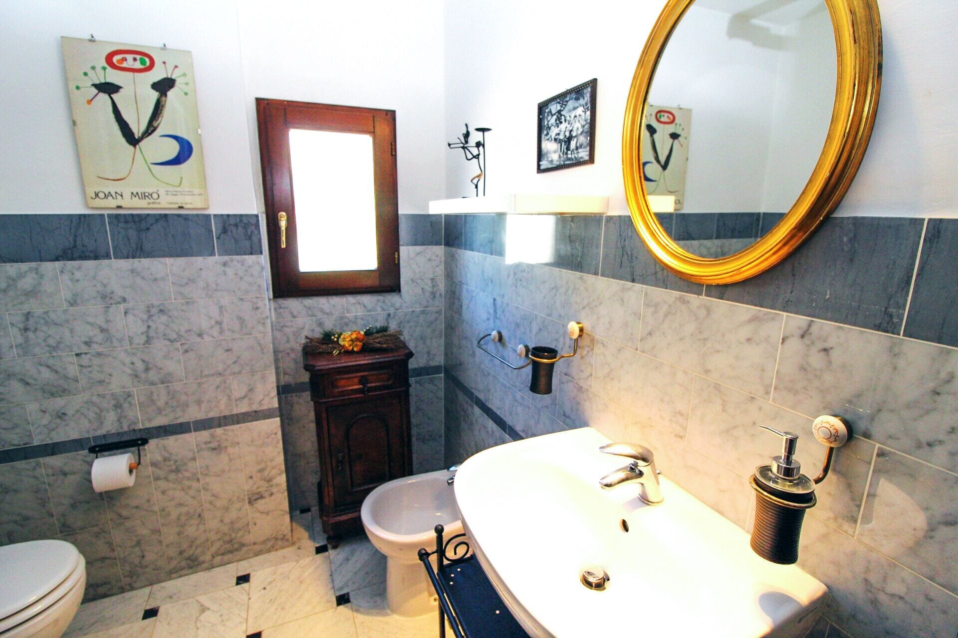 Een badkamer met toilet, wastafel, spiegel en een lijst met een afbeelding aan de muur.