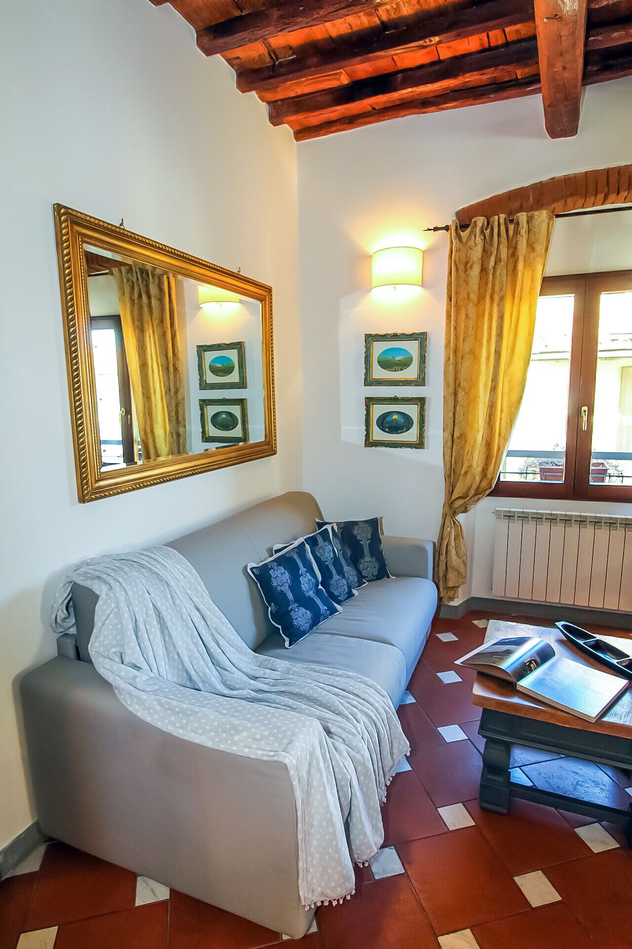 Een gezellige woonkamer met een bank, een grote spiegel, ingelijste foto’s en een raam met gordijnen.