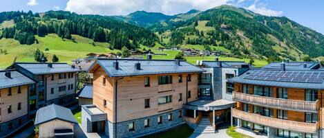 A modern building complex with multiple units, a parking area, and a view of green hills and mountains in the background.