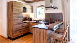 A modern kitchen with wooden cabinetry, a central island, bar stools, and a window providing natural light. - Rauris Penthouse With Sauna (Rauris)
