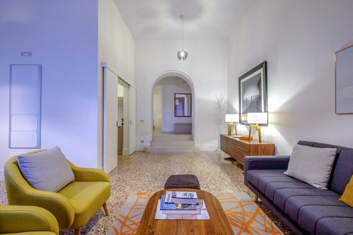 Una sala de estar moderna con sofá, sillón, mesa de centro y un pasillo que conduce a otra habitación.